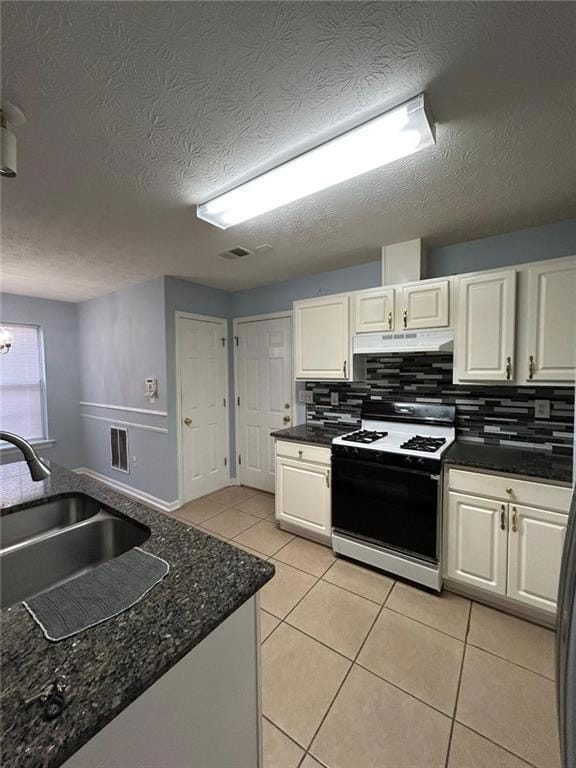 Kitchen with light tile patterned flooring, range with gas stovetop, white cabinetry, tasteful backsplash, and a textured ceiling