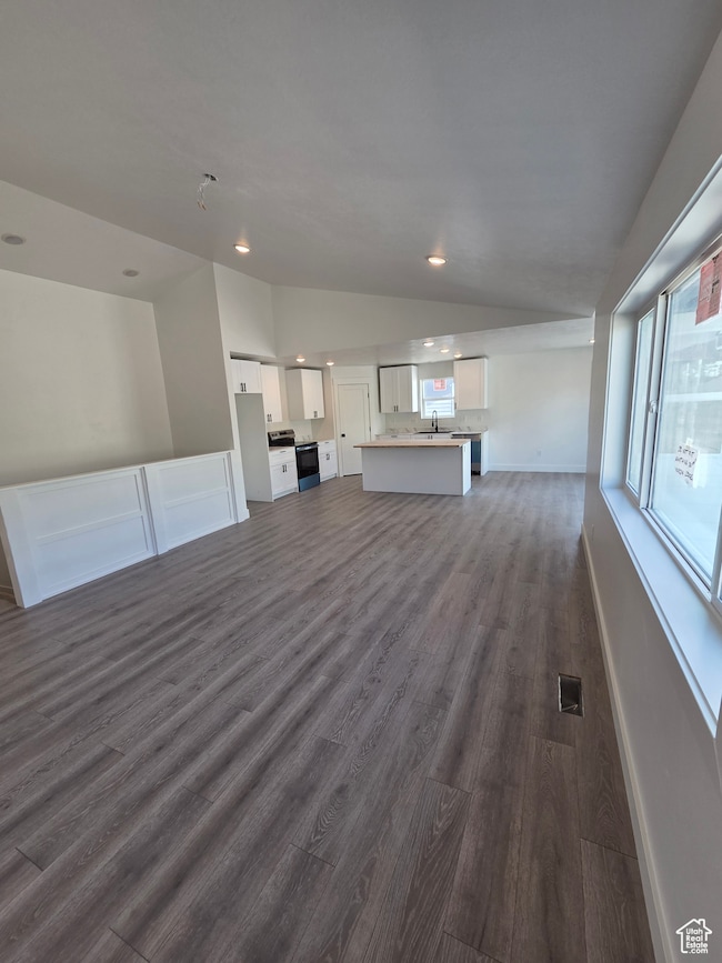 Unfurnished living room featuring vaulted ceiling, a sink, dark wood finished floors, recessed lighting, and baseboards