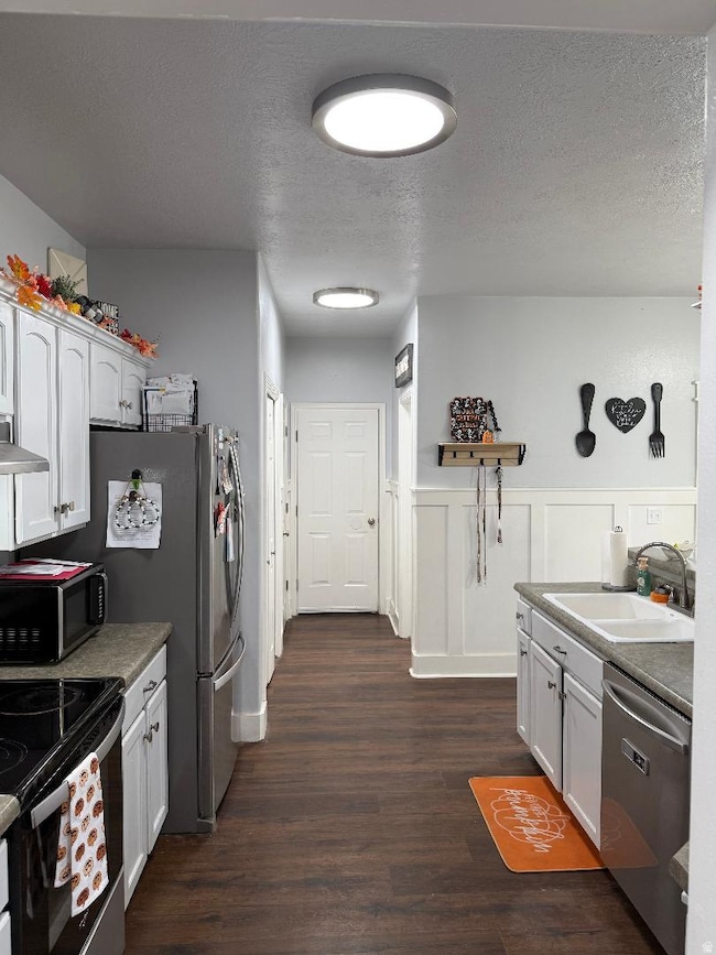 Kitchen with stainless steel appliances, a textured ceiling, white cabinetry, dark wood-style flooring, and dark countertops