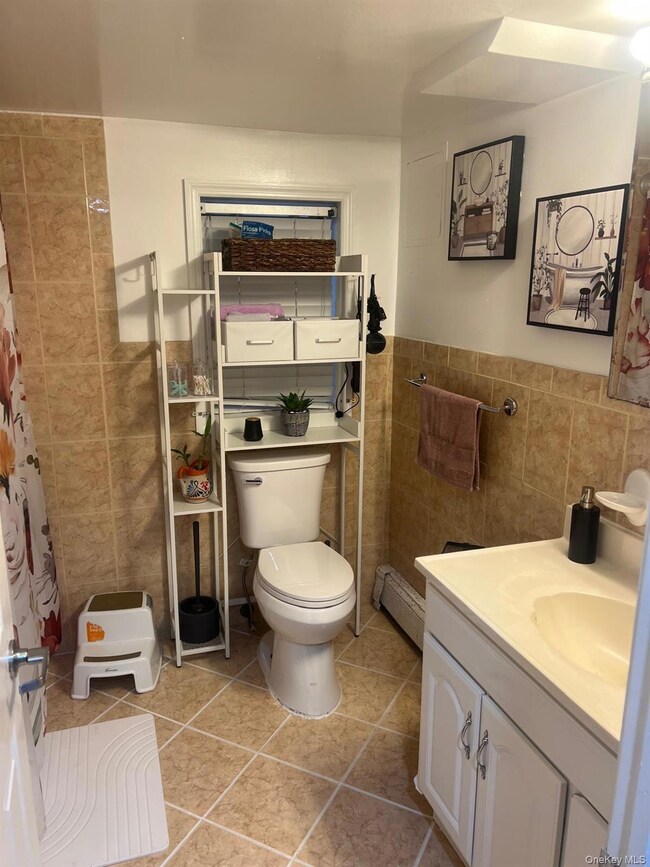 Bathroom with tile walls, a shower with shower curtain, vanity, light tile patterned floors, and a baseboard heating unit