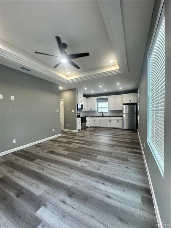 Unfurnished living room with a tray ceiling, ceiling fan, recessed lighting, and crown molding