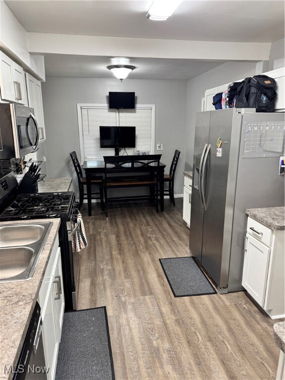 Kitchen with refrigerator, wood finished floors, stove, white cabinetry, and dishwashing machine
