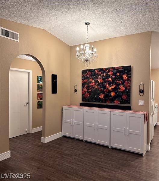 Unfurnished dining area featuring dark wood-style flooring, arched walkways, a chandelier, and a textured ceiling