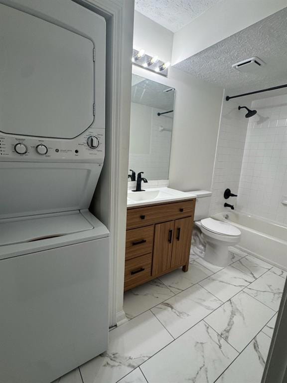Full bath featuring stacked washer / drying machine, vanity, marble look tile flooring, a textured ceiling, and shower / bathtub combination