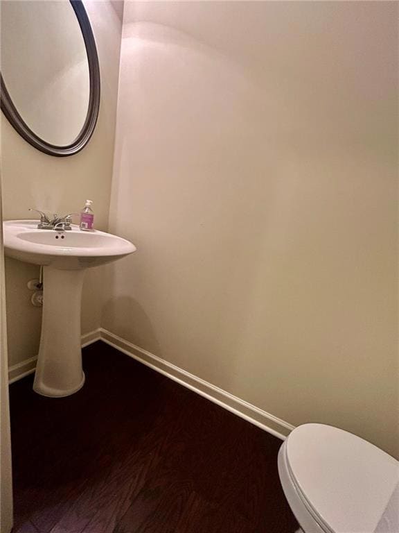 Half bathroom by front door with baseboards, toilet, wood finished floors, and a sink