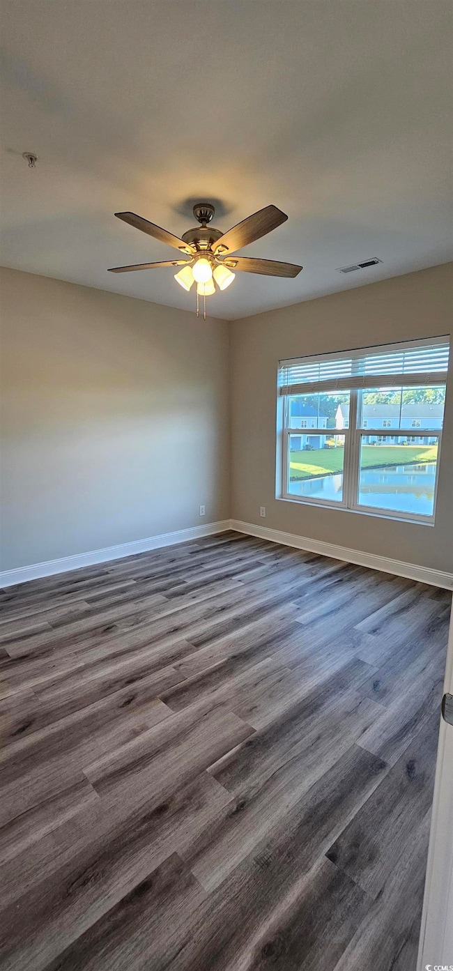 Empty room with a ceiling fan, fire sprinkler in ceiling, and dark wood finished floors
