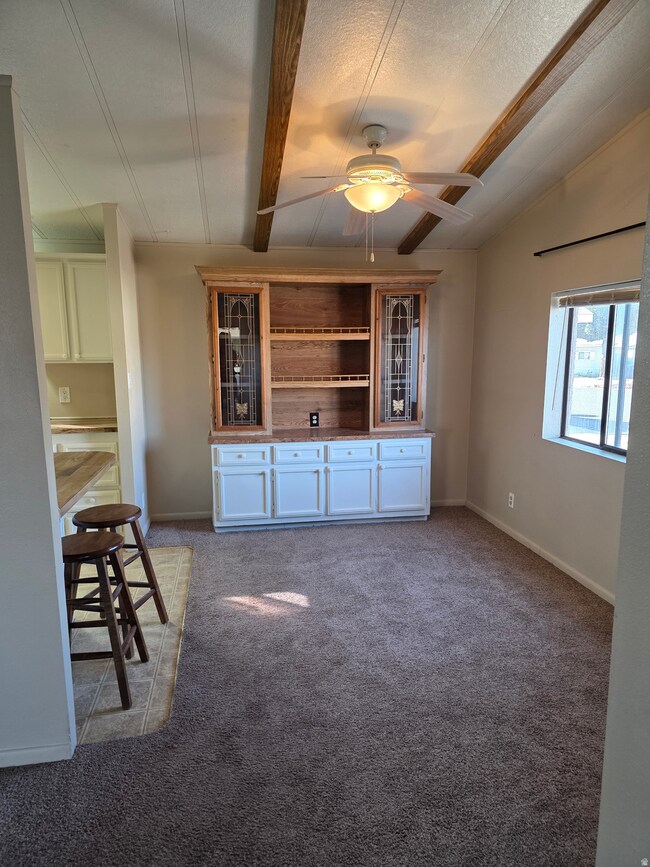 Unfurnished living room with beamed ceiling, light colored carpet, a ceiling fan, and a textured ceiling
