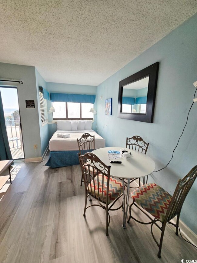 Bedroom with wood finished floors, a textured ceiling, access to outside, and baseboards