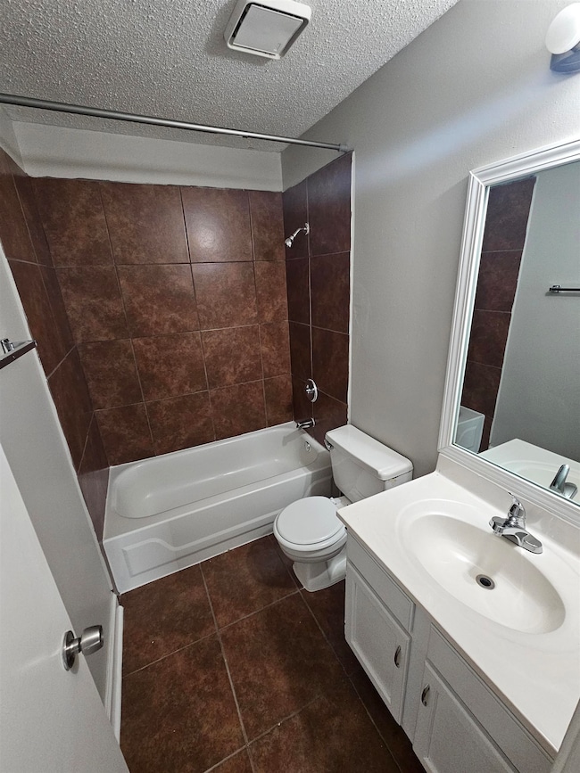 Full bath featuring tub / shower combination, toilet, vanity, tile patterned floors, and a textured ceiling