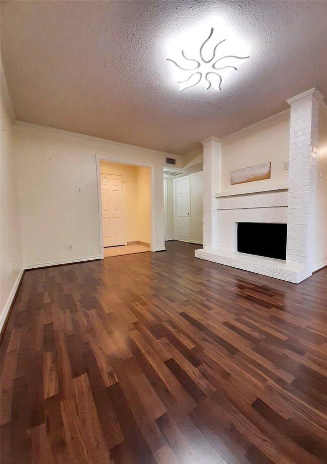 Unfurnished living room with dark wood-type flooring, a textured ceiling, and a brick fireplace