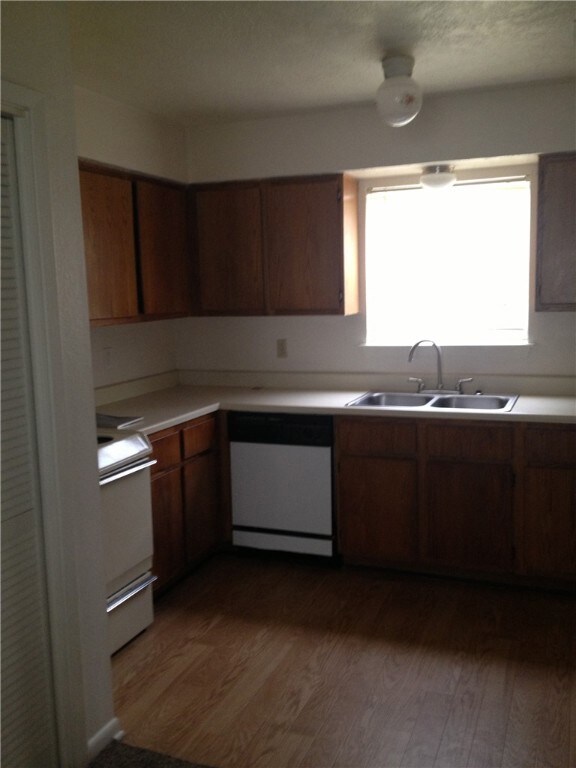 Kitchen with brown cabinets, a sink, light countertops, dark wood-style floors, and white appliances