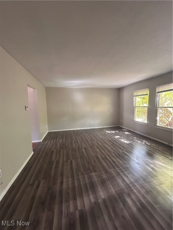 Spare room featuring dark wood-type flooring and baseboards
