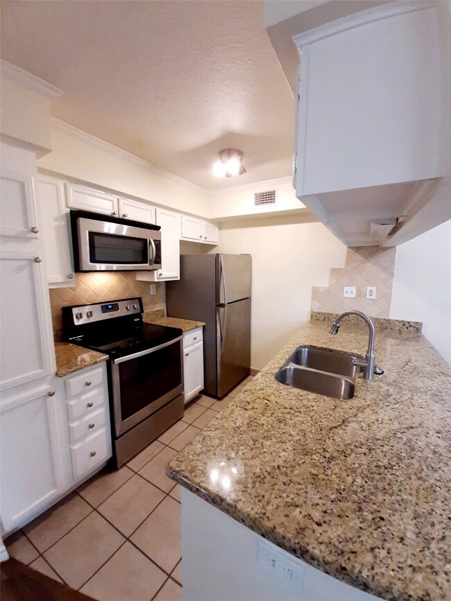 Kitchen featuring backsplash, appliances with stainless steel finishes, white cabinets, light tile patterned flooring, and crown molding