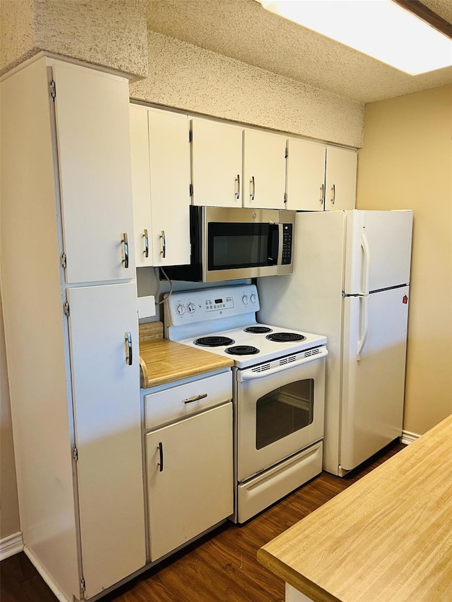 Kitchen featuring white appliances, light countertops, dark wood finished floors, and white cabinetry