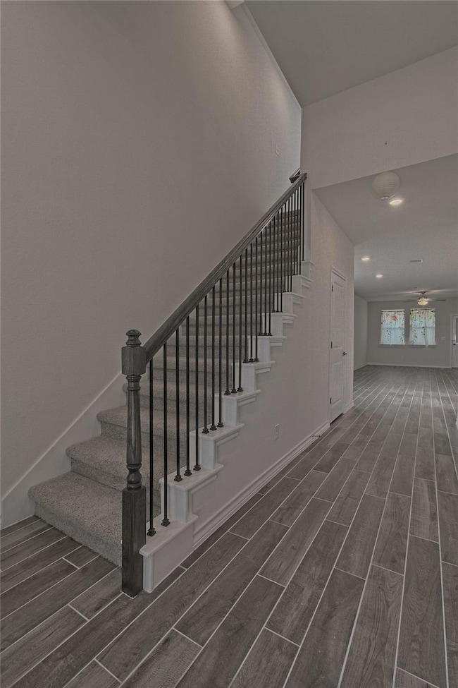 Staircase with wood finish floors, ceiling fan, a