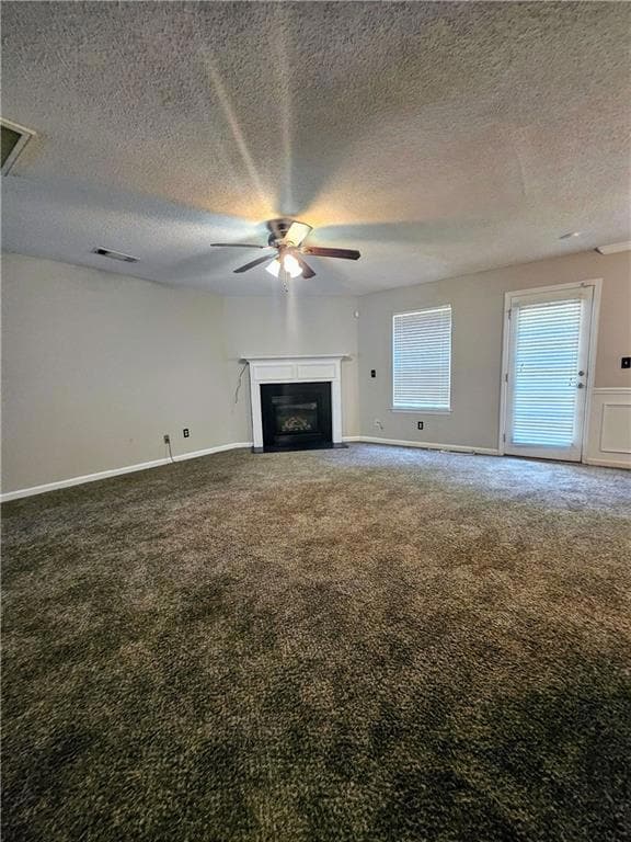 Unfurnished living room with ceiling fan, carpet floors, a fireplace, and a textured ceiling