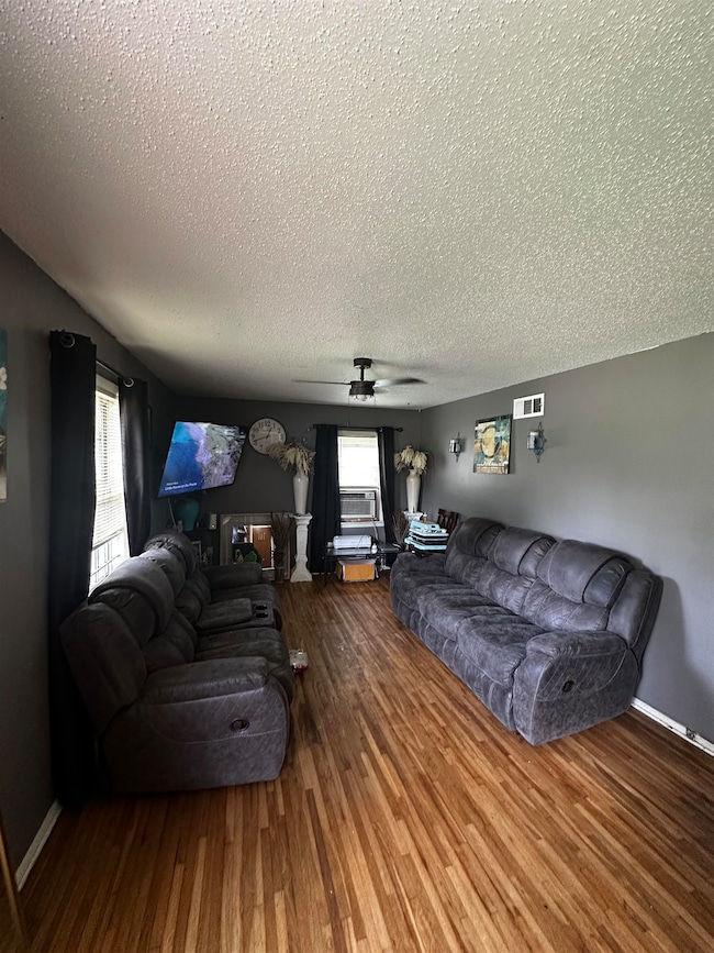 Living room with a textured ceiling, wood finished floors, a ceiling fan, and baseboards