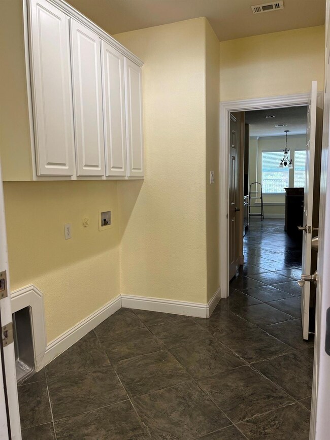 Washroom with hookup for a washing machine, dark tile flooring, a notable chandelier, and cabinets