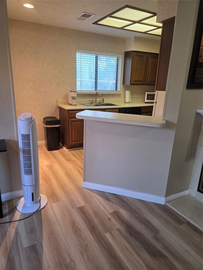 Kitchen with a sink, light wood-style floors, visible vents, light countertops, and baseboards
