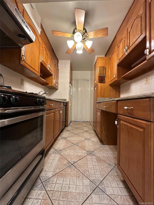 Kitchen featuring stainless steel gas range, exhaust hood, ceiling fan, decorative backsplash, and brown cabinets