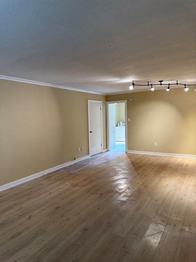 Unfurnished room featuring washer / dryer, wood finished floors, ornamental molding, and a textured ceiling