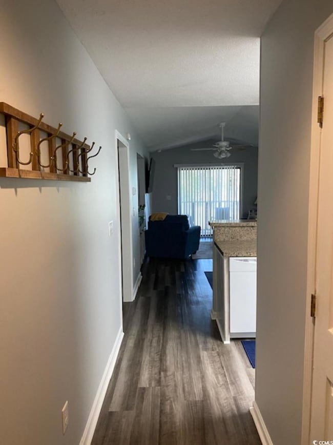 Hallway with dark wood-type flooring, vaulted ceiling, and baseboards