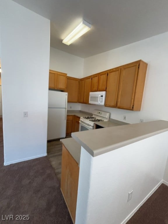 Kitchen with white appliances, a peninsula, light countertops