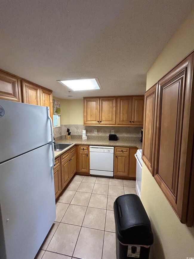 Kitchen featuring a skylight, white appliances, a textured ceiling, and light tile patterned flooring