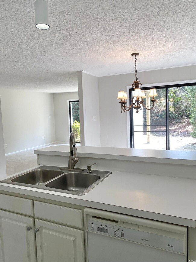 Kitchen with dishwasher, light countertops, an inviting chandelier, a textured ceiling, and a sink
