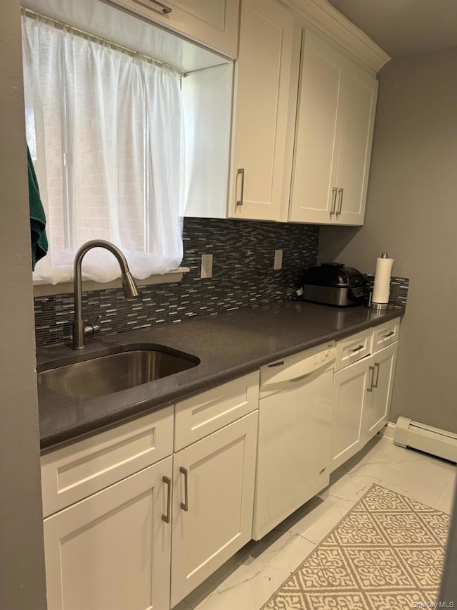 Kitchen featuring light marble finish flooring, white dishwasher, decorative backsplash, white cabinetry, and a baseboard heating unit