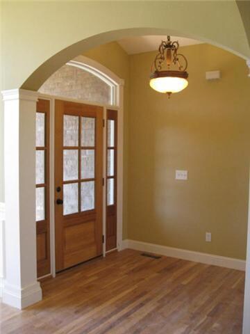 The dramatic arched entryway includes sidelights, a barrel ceiling, trimmed columns, and hardwood floors.