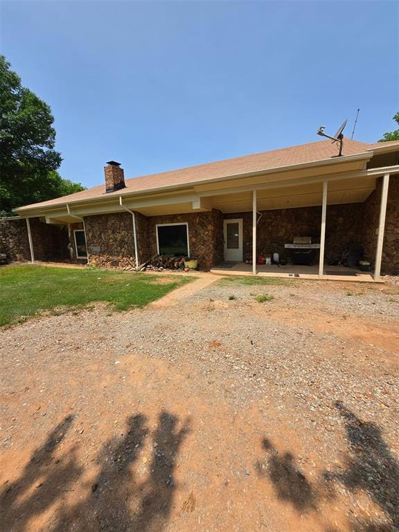 View of front of earth sheltered home featuring stone siding & a chimney.