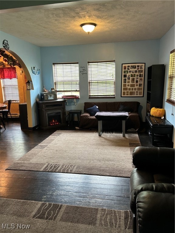 Living room featuring a textured ceiling, arched walkways, a baseboard heating unit, a warm lit fireplace, and hardwood / wood-style floors