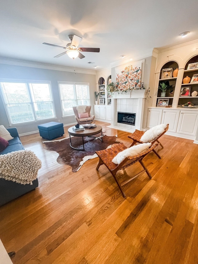 Living room with built in shelves, ceiling fan, hardwood / wood-style flooring, and ornamental molding
