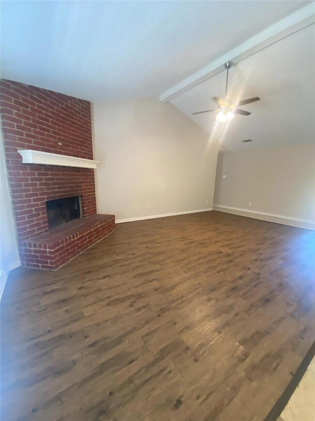 Unfurnished living room featuring ceiling fan, dark wood-type flooring, lofted ceiling with beams, and a brick fireplace