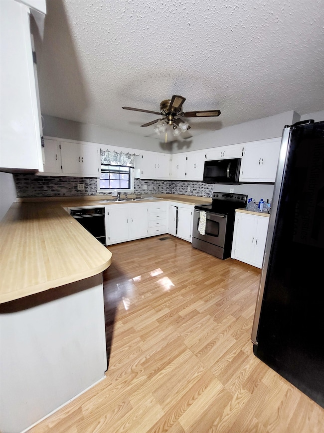 Kitchen featuring black appliances, light wood-style flooring, white cabinets, decorative backsplash, and a textured ceiling