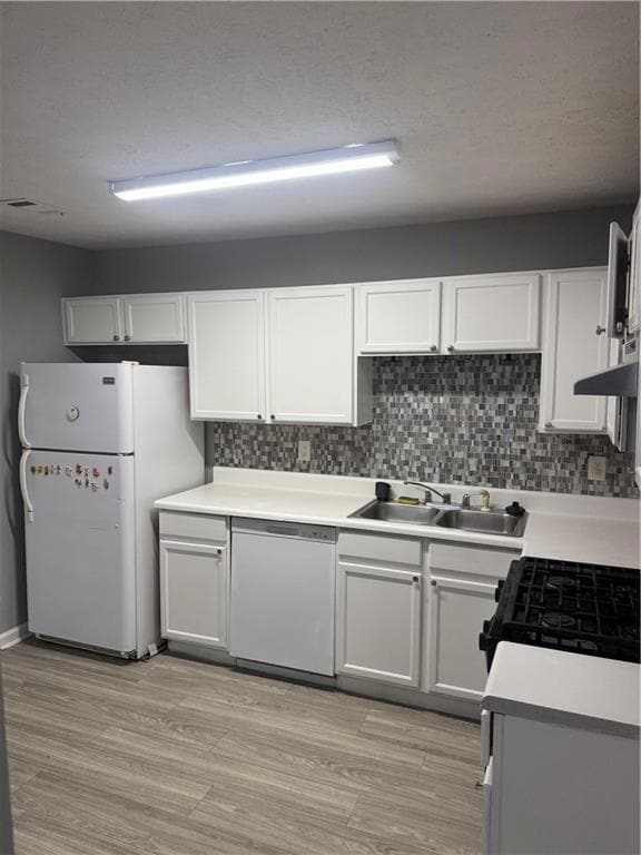 Kitchen featuring tasteful backsplash, refrigerator, light countertops, white dishwasher, and white cabinetry