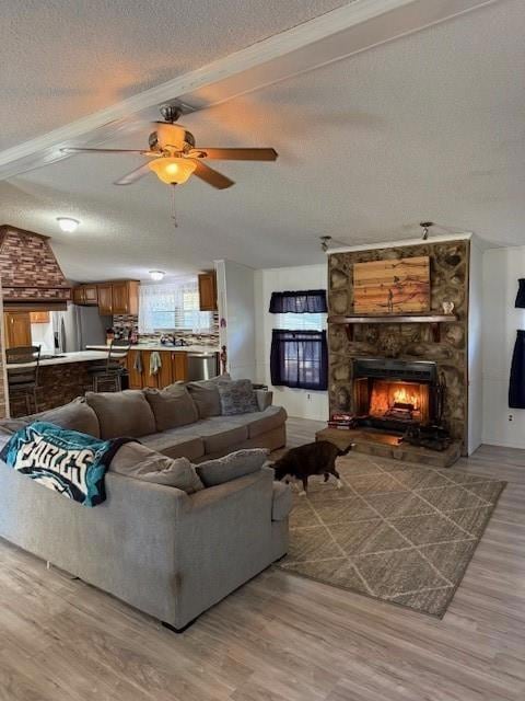 Living room featuring light wood-style floors, a stone fireplace, a textured ceiling, and a ceiling fan