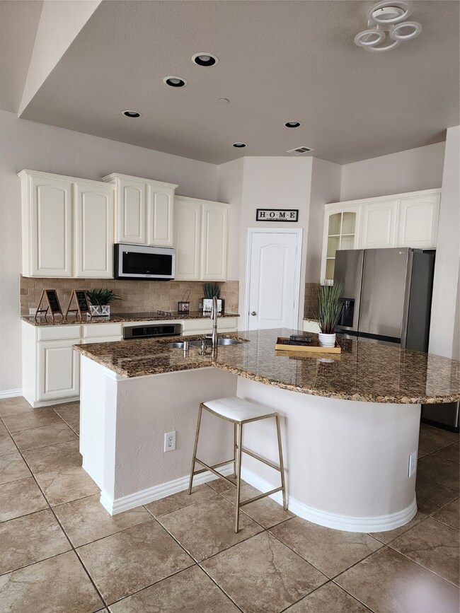 Kitchen with backsplash, a large island with sink, a kitchen bar, white cabinets, and recessed lighting