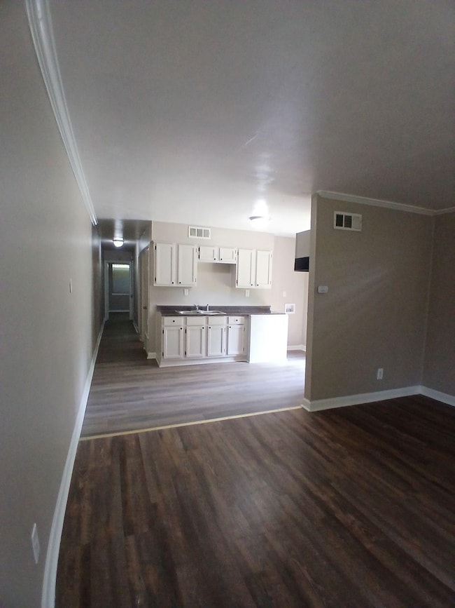 Unfurnished living room with dark wood-type flooring and crown molding