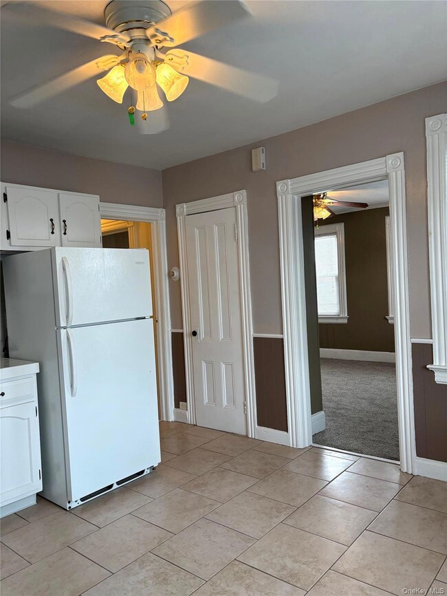 Kitchen with a ceiling fan, freestanding refrigerator, white cabinetry, light tile patterned floors, and light countertops