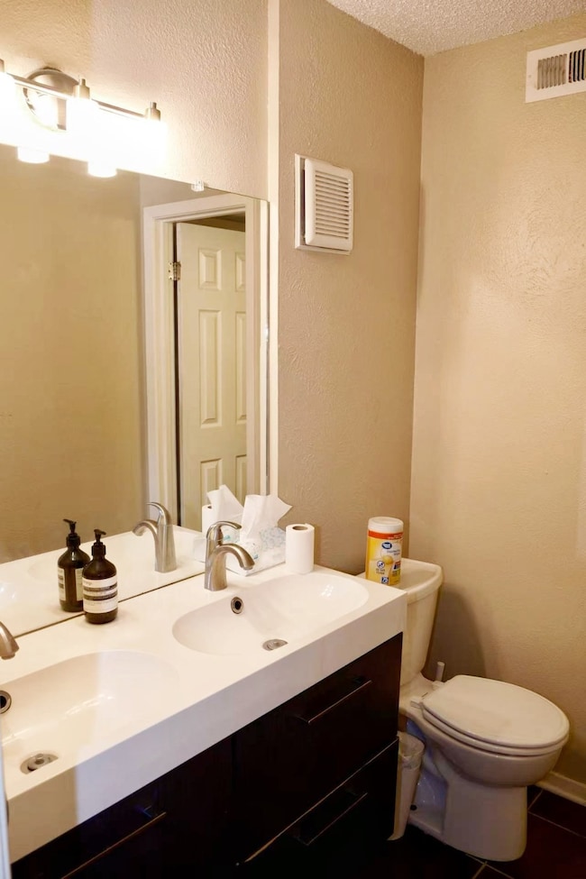 Half bath featuring a textured wall, double vanity, a textured ceiling, and dark tile patterned flooring