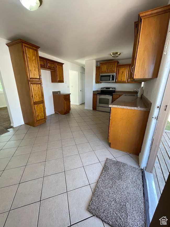 Kitchen with brown cabinetry, appliances with stainless steel finishes, and light tile patterned flooring