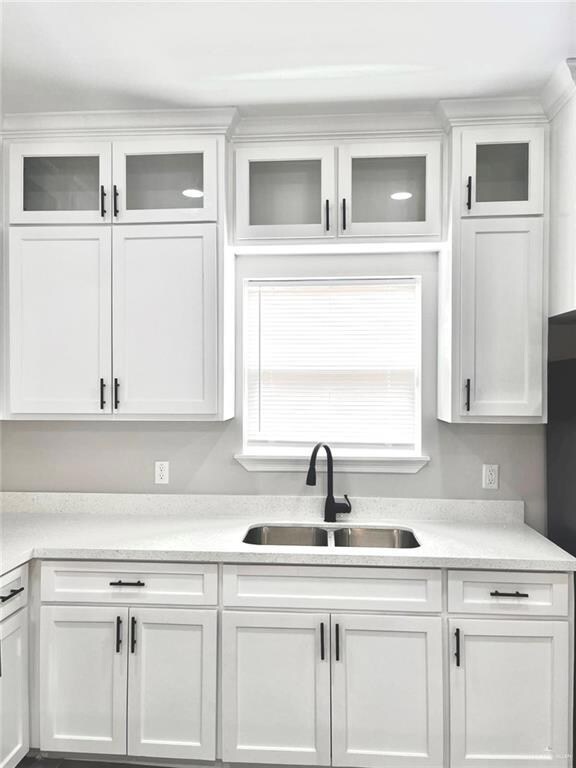 Kitchen featuring glass insert cabinets, white cabinets, and light stone counters