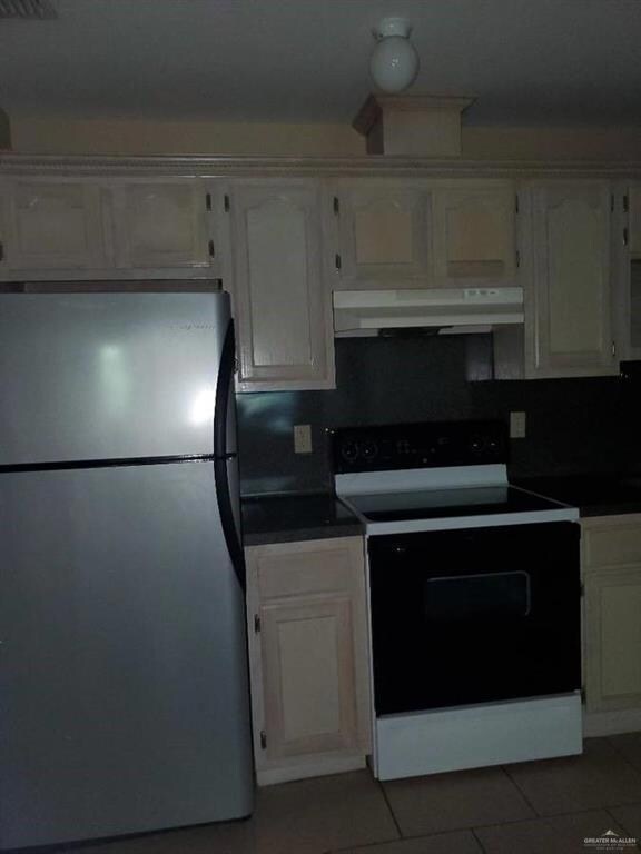 Kitchen with electric stove, tile patterned flooring, white cabinets, and stainless steel refrigerator