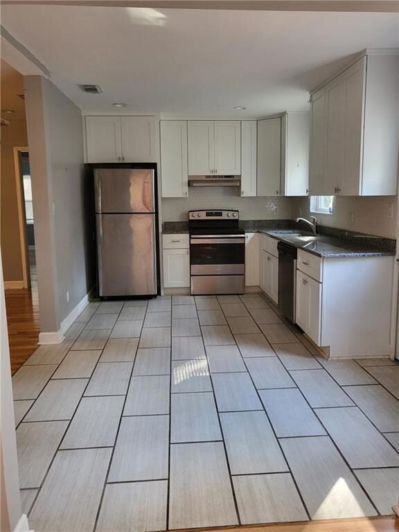 Kitchen with stainless steel appliances, white cabinets, light tile patterned floors, under cabinet range hood, and dark stone counters