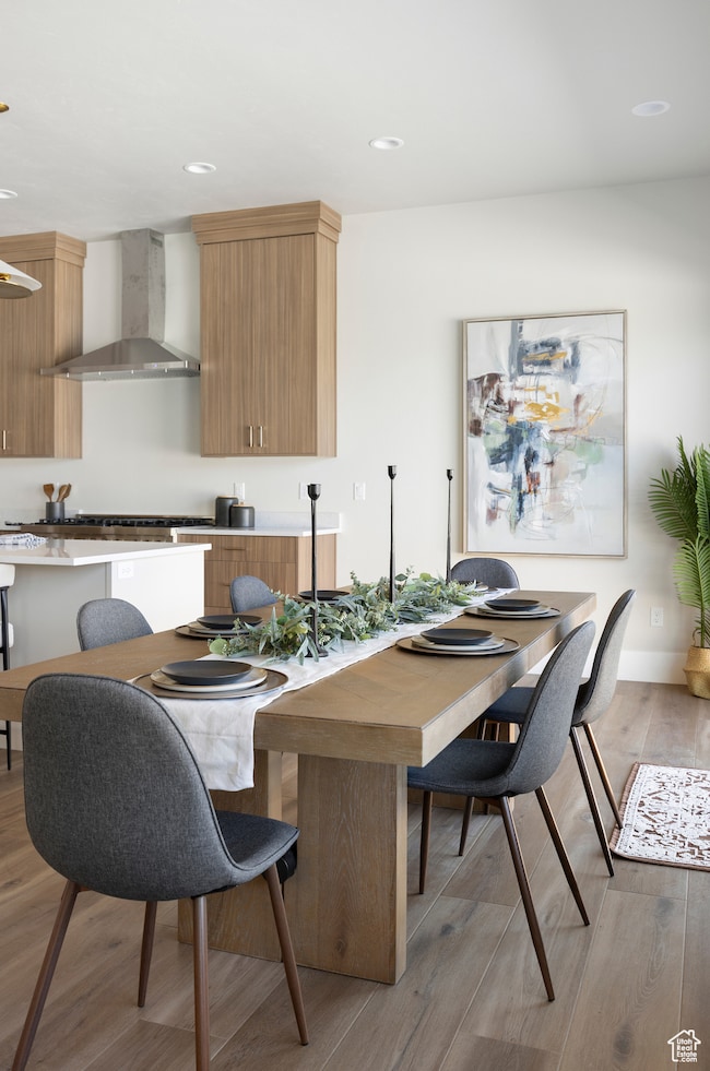 Kitchen featuring light wood-style flooring, wall chimney range hood, recessed lighting, brown cabinetry, and modern cabinets