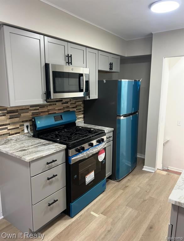 Kitchen with gray cabinetry, range with gas stovetop, stainless steel microwave, tasteful backsplash, and light wood-style floors