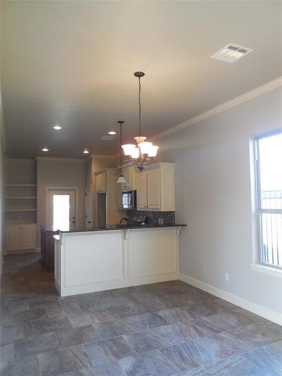 Kitchen with a peninsula, a chandelier, ornamental molding, decorative light fixtures, and stainless steel microwave