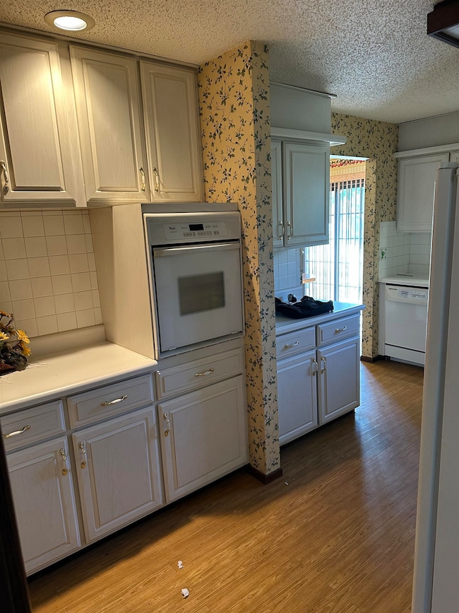 Kitchen with backsplash, light wood-type flooring, light countertops, white appliances, and wallpapered walls